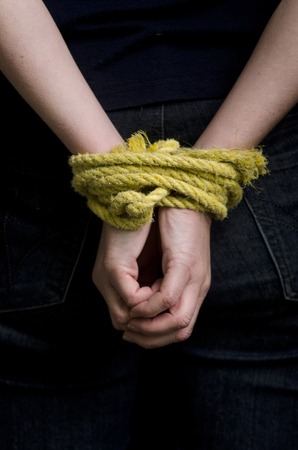 Hands of a missing kidnapped, abused, hostage, victim woman  tied up with rope in emotional stress and pain, afraid, restricted, trapped, call for help, struggle, terrified, locked in a cage cell.の写真素材