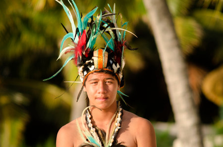 Portrait of attractive young Polynesian Pacific Island Tahitian male dancer in colorful costume dancing on tropical beach during sunset.のeditorial素材