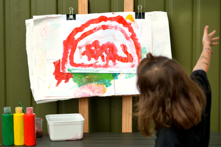 Little artist girl show her finished painting with water colors on large paper canvas outdoor.Concept photo of creativity, talent and imagination in young childrenの写真素材
