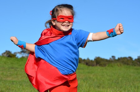 Superhero child (girl) runs against dramatic blue sky outdoor background with copy space. concept photo of Super hero, girl power, play pretend, childhood, imagination.の写真素材