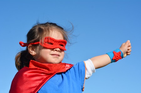 Superhero child (girl)  against dramatic blue sky background with copy space. concept photo of Super hero, girl power, play pretend, childhood, imagination.の写真素材