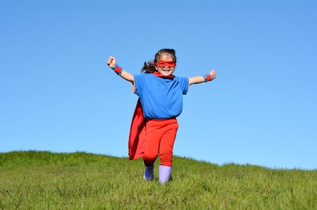 Superhero child (girl) runs against dramatic blue sky outdoor background with copy space. concept photo of Super hero, girl power, play pretend, childhood, imagination.の写真素材