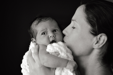 Young mother hold and kiss her newborn baby (3 week old). vertical (BW) copyspace