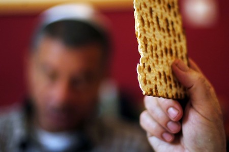 A man is blessing on Matzah (unleavened bread) while another wearing a kippah (scullcap) reads the...