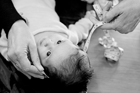 Hands of pediatrician nurse with measuring tape checks infant baby body development examination. Head circumference (BW)の写真素材