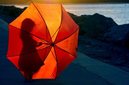 Silhouette of a little girl (age 04) with red umbrella during sunset.の写真素材