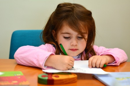 Portrait of a little cild ( girl age 4 ) concentrated while drawing and painting a picture with...