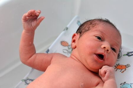 Little newborn baby 14 days old, having his first bath at home.