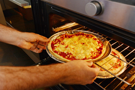 Man hands getting out from the oven a ready homemade pizza.の写真素材