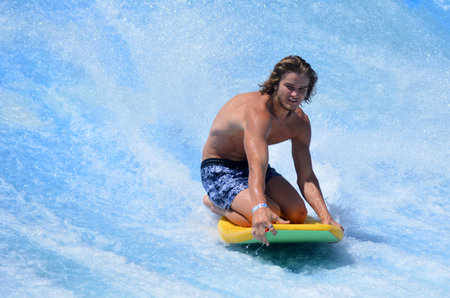 GOLD COAST OCT 29 2014: Young man ride a surfing board on FlowRider. It is a water park attraction that simulate the riding of waves in the oceanのeditorial素材