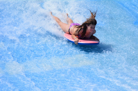 GOLD COAST OCT 29 2014: Young woman ride a surfing board on FlowRider. It is a water park attraction...