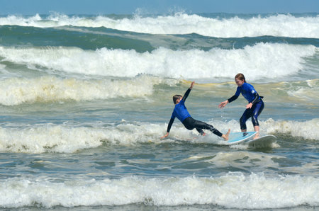MURIWAI, NZL -  JAN 01 2015:Young people surf in Muriwai beach.It's a very popular beach in New Zealand known for it beauty and for its outdoor activities such as swimming, surfing, biking and fishing.のeditorial素材
