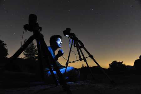 KIRYAT GAT - AUGUST 12: Man gazing out at the night sky and photographing the stars with his cameras on a tripods on August 12 2009 near Kiryat Gat, Israel.It's is a common name for the visible path of a meteoroid as it enters the atmosphere to become a mのeditorial素材