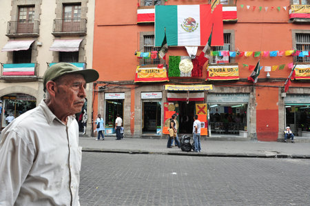 MEXICO CITY - FEB 23 2010:Mexican man pass by the flag of Mexico.Mexico City has the highest elevation and is the oldest city in North America. It is also one of the largest cities in the world.のeditorial素材