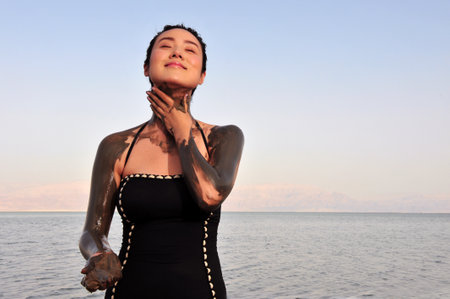 DEAD SEA, ISR - MAY 14:Young Chines woman is enjoys natural mineral mud on May 14 2010.The Dead Sea is filled with minerals including calcium, iodine, saline, potassium, and bromide.のeditorial素材
