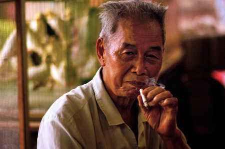 HONG KONG - JULY 09:An old chines man smokes cigaret in the birds market on July 09 2004.Chinese people consume 3 million cigarettes every minute.のeditorial素材