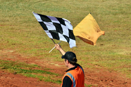 TAIPA, NEW ZEALAND - JUNE 02 2012: A starter  holds a checkered flag and local caution single during a dirt track racing on June 02 2012 in Taipa speedway, New Zealand.のeditorial素材