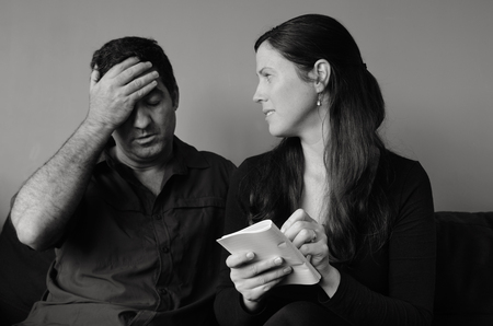 Worried husband and wife  listing expenses in the living room. Spouse relationship concept (BW)の写真素材