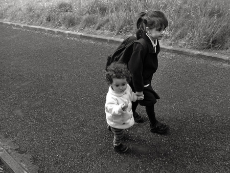 Young sister (girl age 1-5) walks with her older sister (girl age 5-6) to school (BW)の写真素材