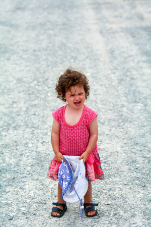 Little girl (age 1-2) having a tantrum screaming alone on a gravel road during holiday travel vacation.Childhood concept with copy spaceの写真素材