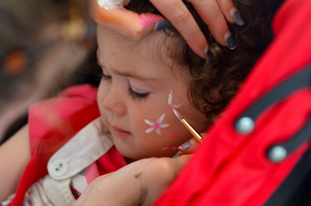Toddler girl age 1-2 getting her face painted with flowers by face painting artist.の写真素材
