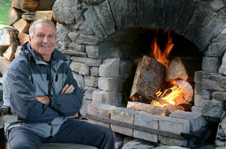 Happy mature man 70's smile near awarm outdoor fireplace.の写真素材