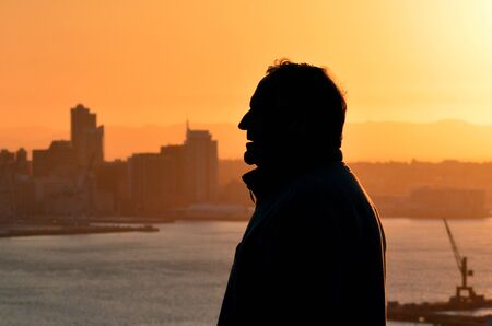Silhouette of mature man against city skyline during sunset.の写真素材