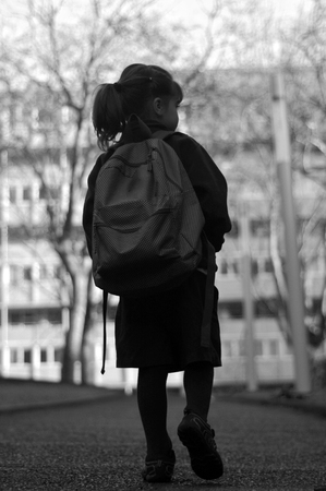 Silhouette back view of a little girl (age 6) with school bag walks to school alone by herself in the street. Education concept. vertical  copy spaceの写真素材