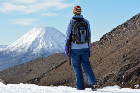 Woman (walks away from camera) hike the Tongariro crossing with Mount Ngauruhoe and Mount Tongariro at the background in Tongariro National Park at the centre of New Zealand's North Islandの写真素材