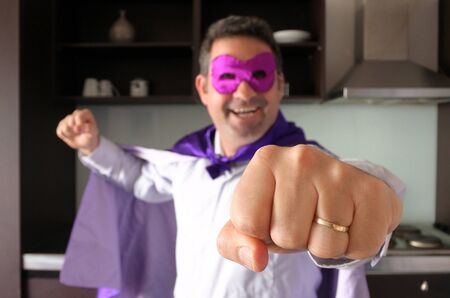 Happy superhero father in home kitchen looking and gesturing with his fist at the camera. Parenthood, fatherhood and father lifestyle concept. real people. copy spaceの写真素材