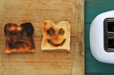 Flat lay view of two slices of toasted bread on a wooden board beside a toaster. One is burned and one is well done. Happiness lifestyle concept. copy spaceの写真素材