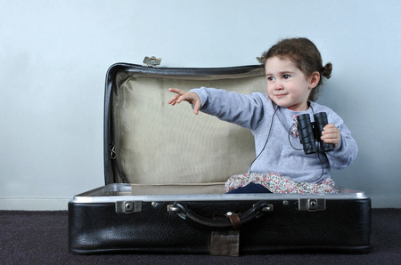Little child (girl age 02) playing at home a kid traveler game in a travel suitcase. Children, travel, holiday, vacation and trip concept.の写真素材