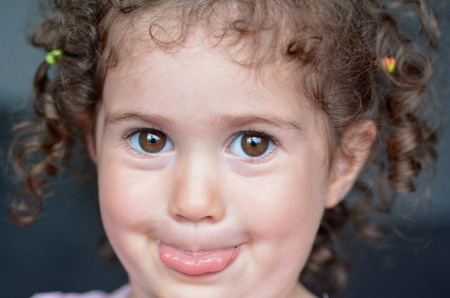 Curly child (girl age 02) sticking a tongue out. Education and childhood concept. Real people. copy spaceの写真素材
