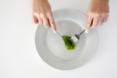 Eating disorder. Cropped image of woman hands eating piece of lettuce. Copy spaceの写真素材