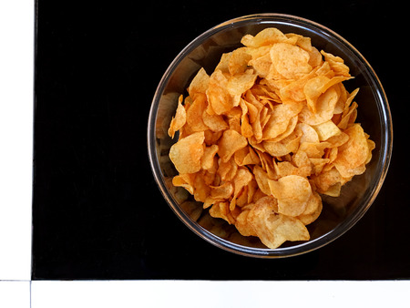 Flat lay view of a bowl full of crispy potato chips served on a living room table. Home party...
