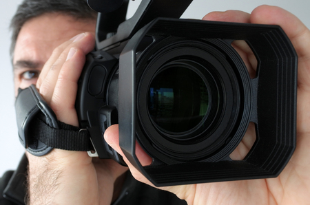 Close up video camera lens with of cameraman face filming with it in the background. Real people.の写真素材