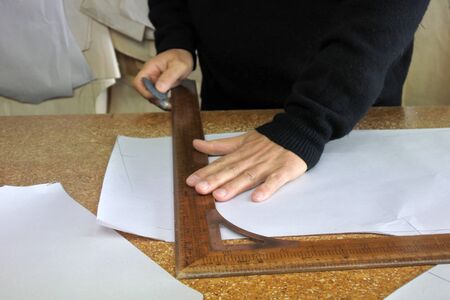 Hands of professional tailor chalking measurements on table in traditional tailors shop studio....