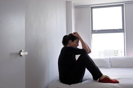 Depressed adult victim woman (age 30-40) sitting and crying on the bed at home, suffering from a...