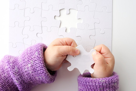 Child hands holds the last puzzle piece of a Jigsaw puzzle. Problem solving concept. Copy spaceの写真素材