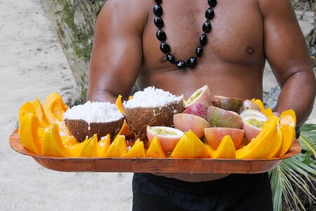 Cook Islander man serves coconut and papaya fruit on a tray in Rarotonga, Cook Islands. Food background and texture. Real people. Copy spaceの写真素材