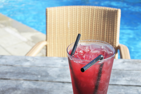 A red cocktail drink with ice served on a poolside table in a tropical resort.Travel holiday...