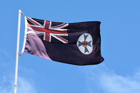 The state flag of Queensland Australia on a pole flying against blue sky.の写真素材
