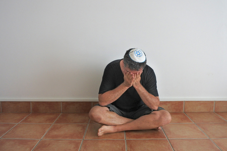 Jewish man sitting on the ground in his home during shiva, the week-long mourning period in Judaism for first-degree relatives that passed away.の写真素材