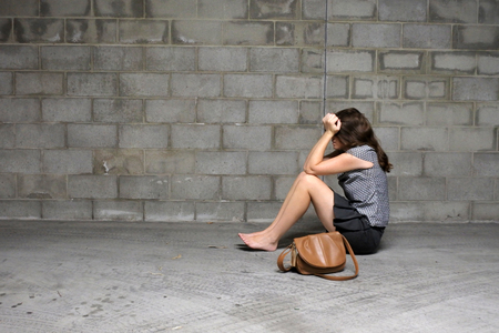 Upset young woman sits on the ground in an underground carpark after being attacked by a manの写真素材