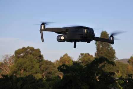 Drone flying fast above treetops at sunset.