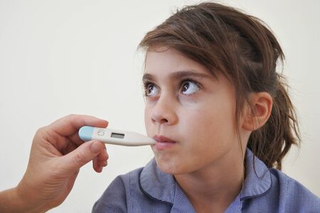 Medical person measuring temperature to a sick young schoolgirl. Real people. Copy space