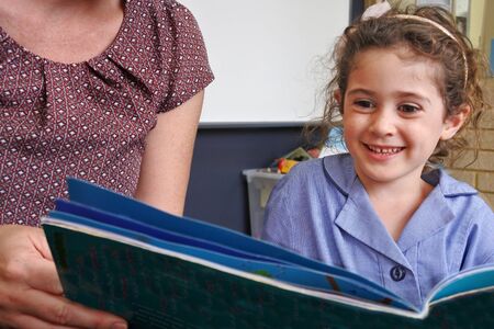 Young Australian school girl (age 5-6) listening to a teacher book reading in classroom. Real...