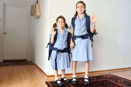 Two happy sisters (age 10 and 6) looking at camera and waving goodbye to parents before going to...