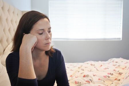 Upset adult woman sitting on bed in bedroom.