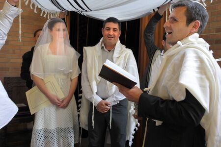 Rabbi blessing Jewish bride and a bridegroom in modern Orthodox Jewish wedding ceremony in synagogue.Real people. Copy spaceの写真素材